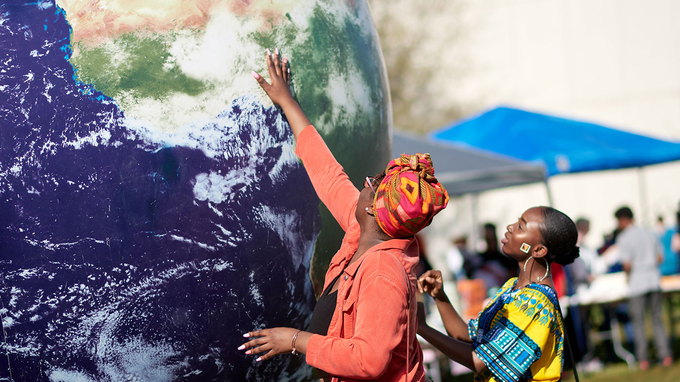 two women reaching up towards Africa on a huge globe at iFest.