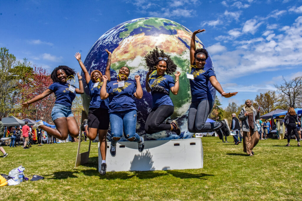 five happy students jump for joy in front of a huge globe during the international festival at UNCG.