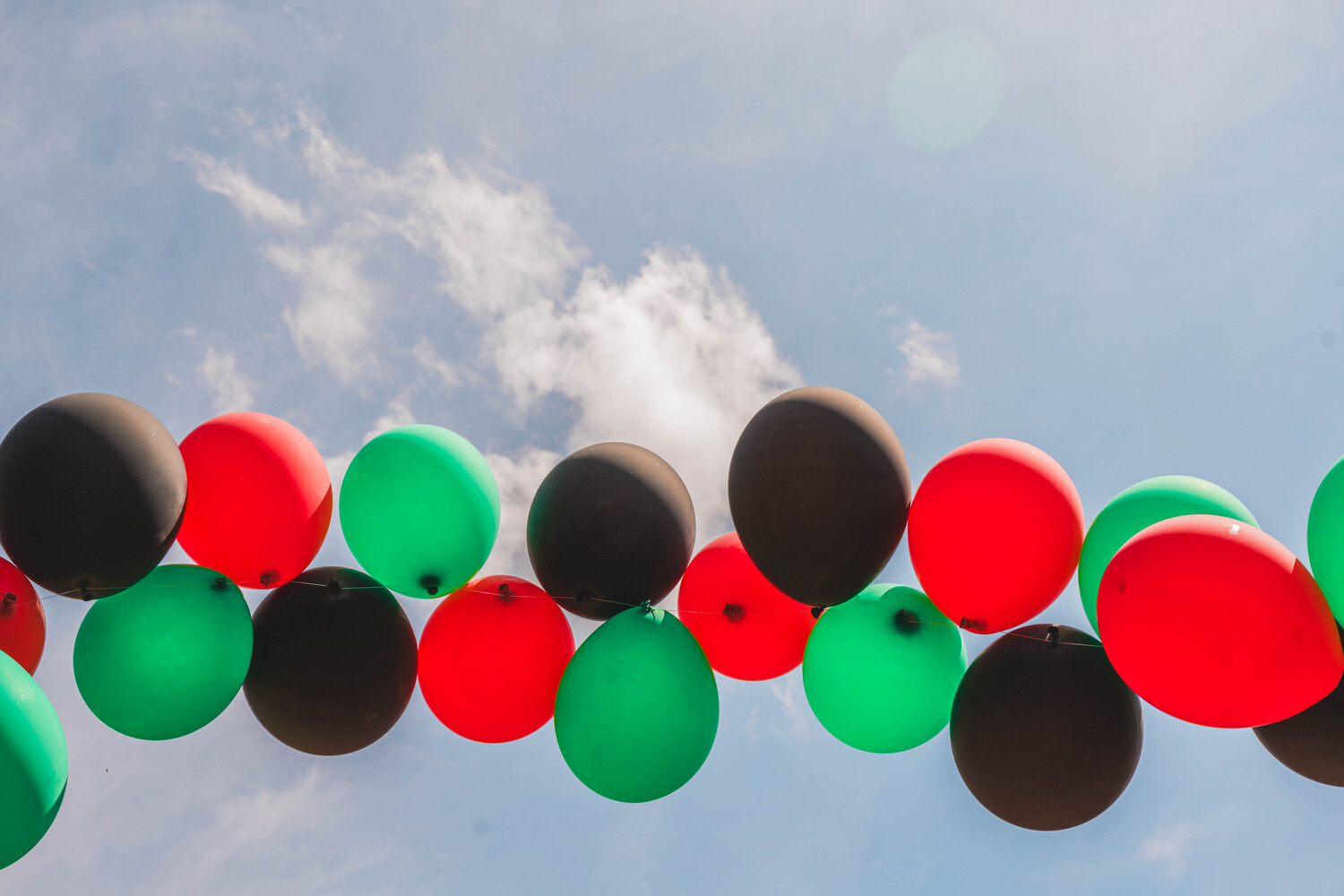 Red, Black, and Green balloons under a sunny sky for a Juneteenth celebration.